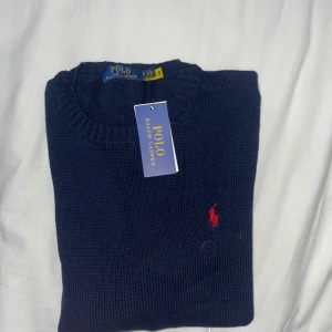 Mörkblå stickad tröja Polo Ralph Lauren - Accepterar många bud !Mörkblå stickad tröja från Polo Ralph Lauren med klassisk rund halsringning och röd broderad logga på bröstet. Tröjan är i bomull och har en enkel, stilren design som passar perfekt till jeans eller chinos.