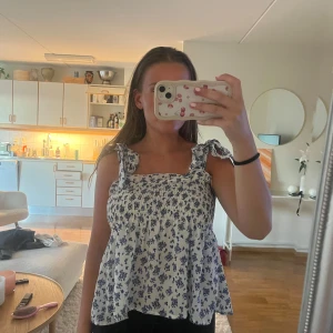 Vit blommig linnetopp med knytband - Supersöt vit linnetopp med blått blommönster. Axelbanden knyts i rosetter för en gullig touch. 