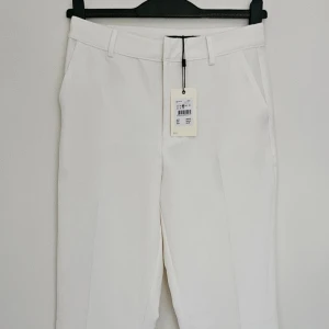 Vita kostymbyxor - Vita kostymbyxor från BikBok, stl 38                           Helt oanvända, taggen sitter kvar.  Tunt luftigt polyestertyg med pressveck framtill.   