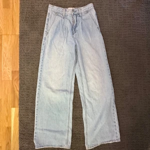 Ljusblå wide jeans från Stradivarius - Säljer ett par ljusblå jeans från Stradivarius i storlek 34. Jeansen har en wide passform med raka, vida ben och klassisk femficksdesign. Tillverkade i jeansmaterial med dragkedja och knapp framtill. Perfekta för en avslappnad och trendig look.