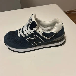 New Balance 574 marinblå sneakers - Snygga New Balance 574 sneakers i marinblå mocka och mesh med vita detaljer och snörning. Klassisk retrostil med vit sula och stor N-logga på sidan. 