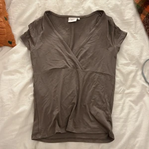 Brun omlottopp från Nelly - Säljer en brun omlottopp från Nelly. Toppen har korta ärmar och en snygg v-ringning framtill. Aldrig andvänd 