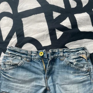 Replay blå jeansshorts med dragkedjor - Snygga blå jeansshorts från Replay med slitna detaljer och råa kanter. Baksidan har två fickor med gula dragkedjor. W30 Legth 30, dom passar mig lite stort som har S