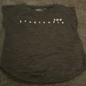 Svart sportig t-shirt från SOC - Svart t-shirt från SOC med trycket 'SPORTSWEAR' framtill. Modellen är kortärmad och har en rundad nederkant. Materialet är lätt och andas, perfekt för träning eller aktiva dagar. Enkel och stilren design som passar till sportiga outfits.