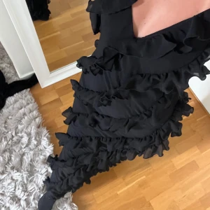 Svart volangklänning från NA-KD - Supersnygg lång svart klänning från NA-KD med tunna axelband och massor av volanger över hela klänningen. V-ringad framtill och figurnära passform.