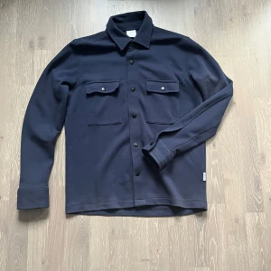 Mörkblå overshirt  - Snygg mörkblå overshirt från Selected Homme i riktigt bra skick. Overshirten har en rak passform och långa ärmar med knapp vid manschetten. Perfekt att ha över en hoodie eller t shirt nu till hösten! Priset kan diskuteras vid snabb affär!      Vid frågor är det bara att höra av sig.