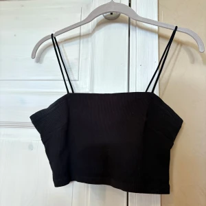Svart croppad topp - Säljer en svart croppad topp från Gina Tricot med tunna axelband. Storleken är en L, MEN passar utmärkt för en M också! Toppen är ärmlös och har en enkel, stilren design som passar perfekt till höga jeans eller kjol. Materialet är mjukt och stretchigt!