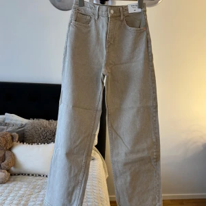 Beige wide leg jeans från H&M - Snygga beige jeans från H&M med wide leg och hög midja. Byxorna har justerbar midja, klassiska fem fickor och raka, vida ben. Perfekta för en chill och trendig look. Materialet är bomull och de har en stilren, enkel design.
