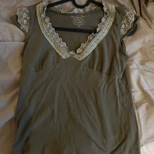 Olivgrön blus med spetsdetaljer - Supersöt olivgrön blus med v-ringning och ljusa spetsdetaljer längs halsringningen och ärmsluten. Knappt använd.