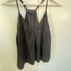 Svart linnetopp med spetsdetaljer - Svart linnetopp från Etam med tunna axelband och snygga virkade spetsdetaljer framtill och bak. Toppen har en lös passform och faller fint, perfekt för varma dagar. Luftigt material och v-ringad skärning framtill ger en avslappnad vibe. Jag använder xs/s, säljer då den inte används längre💗