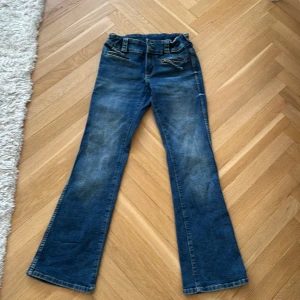 Blå bootcut jeans med dragkedjor från HM - Snygga blå jeans med bootcut passform och coola dragkedjedetaljer framtill. Jeansen har klassisk femficksdesign, markerad midja och lätt slitna partier för en trendig look. Perfekta för dig som gillar en retrostil med modern twist.