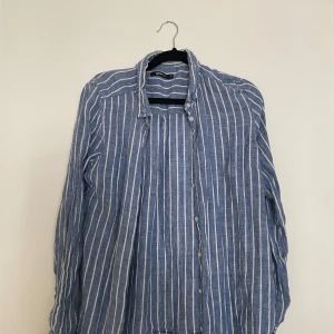 Blåvit randig linneskjorta Gina Tricot - Snygg blå skjorta med vita ränder från Gina Tricot. Skjortan är i luftig linnemix, har lång ärm, klassisk krage och knäppning framtill. Perfekt för en chill och stilren look under varmare dagar.