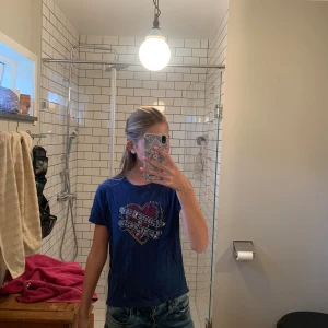 Blå t-shirt Zadig & Voltaire hjärtmotiv - Snygg blå t-shirt från Zadig & Voltaire med ett coolt hjärtmotiv och text framtill i glittriga stenar. Klassisk rund halsringning och korta ärmar. Perfekt till jeans för en avslappnad men trendig look. Några diamanter har trillat av så det är lite borta på några ställen. Men inget som man ser om man kollar långt ifrån.