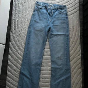 Ljusblå straight jeans från Bershka, M - Säljer ett par ljusblå straight fit jeans från Bershka. Klassisk femficksmodell med normalhög midja och raka ben. Jeansen är i mjuk denim och har snygga detaljer som metallknapp och bälteshällor. Jeansen är helt slutsålda och säljer därför dem för 250kr då nypris var 389kr