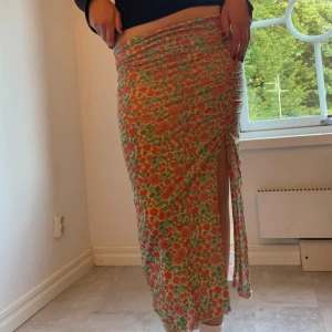 Blommig långkjol med slits från Monki - Supersöt tight långkjol från Monki i blommigt mönster med rosa, röda och gröna toner. Kjolen har en snygg slits på sidan och är gjord i stretchigt tyg. Färg och mönster. 