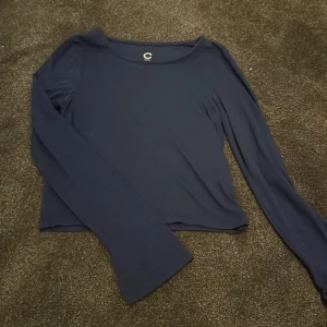 Mörkblå långärmad topp från C - Snygg mörkblå långärmad topp från C i mjukt och stretchigt material. Modellen är croppad med slits vid ärmsluten för en cool detalj. Perfekt att matcha med jeans eller kjol för en chill look.