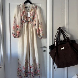 Blommig långklänning från Neo Noir - Superfin långklänning från Neo Noir i ljusbeige med blommigt mönster i rosa, gul och blå. Klänningen har v-ringning, långa puffärmar och flowy passform. 