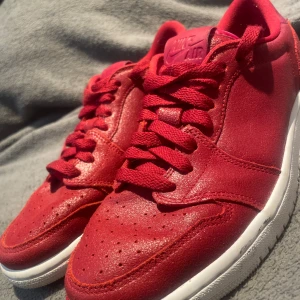 Nike Low Röd - Snygga Nike Air Jordan 1 Low i helrött skinn med matchande röda skosnören och vit sula. Klassisk siluett med perforerad tå och ikonisk Jumpman-logga på innersulan. Perfekta för dig som vill sticka ut med färg på fötterna.