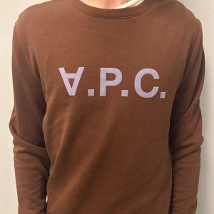 A.P.C. Tröja - Säljer en brun sweatshirt från A.P.C. med stor vit logga framtill. Tröjan har rund halsringning och långa ärmar. Tillverkad i mjuk bomull som är skön att bära. Perfekt för dig som gillar stilren och enkel design. Skick 10/10 fast priset kan förhandlas 