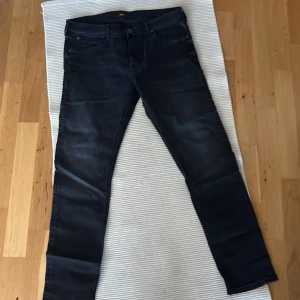 Svarta gråa  jeansbyxor från Lee - Snygga svarta jeansbyxor från Lee med en modern passform. Byxorna har en klassisk design med fem fickor och knappgylf. Perfekta för en stilren look.