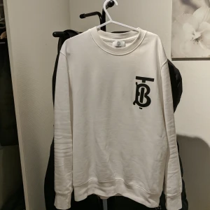 Vit sweatshirt från Burberry - Säljer en stilren vit sweatshirt från Burberry med ett svart tryck på bröstet. Tröjan har långa ärmar och en klassisk rund halsringning. Perfekt för en avslappnad och trendig look.Det ni ser på bilden är det ni får😁 ett plagg som är köpt i bulk så jag vet lila lite som ni, men jag har kollat så gott jag kan på alla möjliga sajter och det jag kan kolla stämmer överens med originalet väldigt bra tröja raka o fina sömmar, kvalitets tyg