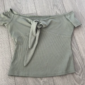 Grön ribbad offshoulder topp - Snygg grön ribbad offshoulder topp med knyt framtill. Perfekt för en stilren look. Kortärmad design som ger en trendig touch.