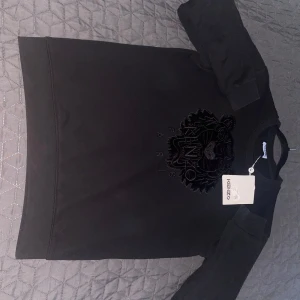 Svart tröja Kenzo - Säljer en svart tröja från Kenzo med ett stort broderat tigerhuvud på framsidan. Tröjan har en normal passform och är perfekt för en stilren look. Märkets logga syns tydligt under tigern. Passar bra till både vardag och speciella tillfällen.
