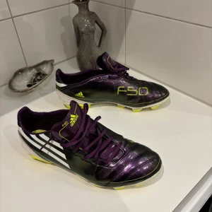 Adidas F50 fotbollsskor - Snygga Adidas F50 fotbollsskor i en cool lila och svart färgkombination med gula detaljer. Denna modell är från 2010 och är riktigt sköna, som dem gamla klassiska skorna alltid var. Inte fått användning av dessa då de blev försmå alldeles för snabbt. Hör av dig!