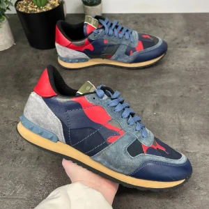 Valentino Rockrunner sneakers i blått och rött - Snygga Valentino Rockrunner sneakers med ett coolt kamouflagemönster i blått, rött och grått. Skorna har snörning och en bekväm sula. Perfekta för att ge din outfit en unik touch.