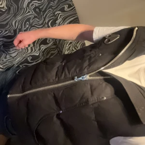 Svart dunväst från Moose Knuckles - Tjenixen! Säljer nu min snygga svarta dunväst som inte går att få tag på igen ifrån Moose Knuckles med dragkedja och logotypdetaljer som passar perfekt för kyligare dagar med sin quiltade design. Västen har en stilren look och är lätt att matcha med olika outfits! Anledningen till varför jag säljer den är för att den inte riktigt matchar min garderob längre och den är köpt på johnells förra året i juli men väldigt sparsamt använd.