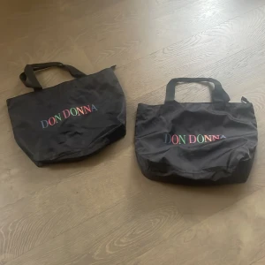 Svart shoppingväska från Don Donna - Säljer en svart shoppingväska från Don Donna med färgglad logotyp på framsidan. Väskan har två handtag och är perfekt för att bära med sig det nödvändigaste. Enkel och stilren design som passar till många tillfällen. 300 kr st❤️