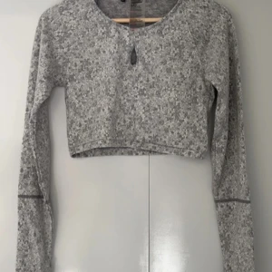 Grå croppad tröja från Gymshark Medium - Säljer en grå croppad tröja från Gymshark med långärmad design. Tröjan har ett diskret mönster och en liten öppning framtill. Använd en gång.