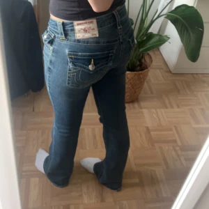 joey flare low blåa jeans med gul sömn från true religion  - Snygga blå jeansbyxor från True Religion med låg midja och bootcut-stil. Byxorna har gula sömmar och knappar på bakfickorna. De är lågmidjade flare/bootcut jeans. De är varsamt andvända och har inga defekter