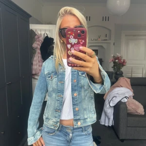 Ljusblå jeansjacka - Säljer en snygg ljusblå jeansjacka med knappar framtill. Jackan har en klassisk design med två bröstfickor och långa ärmar. Perfekt för en avslappnad stil.