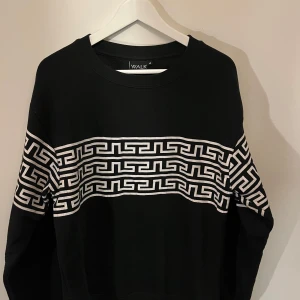 Svart tröja med mönster från Walk - Snygg svart tröja från Walk med ett unikt vitt geometriskt mönster över bröstet och ärmarna. Perfekt för en stilren look. Tröjan har långa ärmar och en bekväm passform.