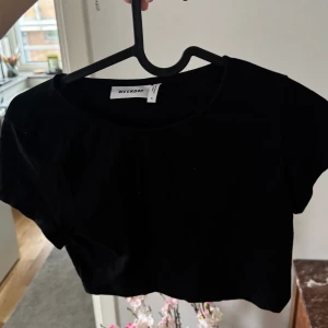 Svart croppad t-shirt från Weekday - Säljer en svart croppad t-shirt från Weekday. Den har en enkel design med korta ärmar och rund halsringning. Perfekt för en avslappnad stil.