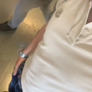 Vit pikétröja med emblem - Snygg vit moncler pikétröja . Perfekt för en stilren look. Knappt använd och köpt från merchsweden! Hör av er vid frågor!