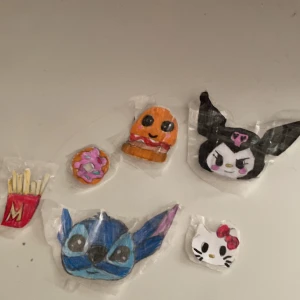 Handgjorda klistermärken med tecknade figurer - Unika handgjorda klistermärken med motiv av tecknade figurer. Inkluderar en blå figur med stora öron och en vit figur med röd rosett. Perfekta för att dekorera anteckningsböcker eller andra ytor.