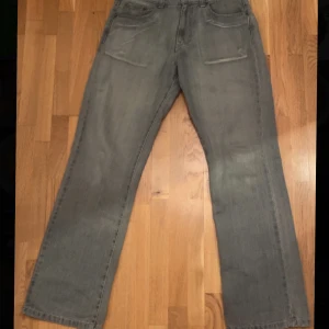 Grå jeans - Säljer ett par grå jeansbyxor. De har en klassisk femficksdesign och en rak passform. Perfekta för en avslappnad stil. Midjan är normalhög och byxorna har en dragkedja och knapp framtill.