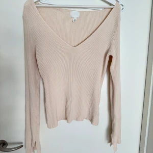 Beige ribbad tröja från H&M - Säljer en stilren beige ribbad tröja från H&M med v-ringning och långa ärmar. Perfekt för en chic och enkel look. Tröjan har en mjuk och bekväm passform.