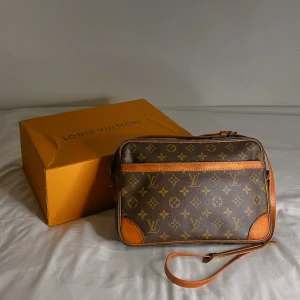 Monogram axelväska från Louis Vuitton trocadero 27 - Säljer en klassisk axelväska från Louis Vuitton med det ikoniska monogrammönstret. Väskan har bruna läderdetaljer och en justerbar axelrem. ”Modellen heter Trocadero 27” och är vintage Perfekt för att ge din outfit en lyxig touch. Liten slitning på ena remen på sidan av väskan med är hållbar går även att Fixa på Louis Vuitton butiken eller en skomakare. 