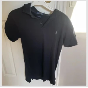 Svart pikétröja från Ralph Lauren - S - Säljer en klassisk svart pikétröja från Ralph Lauren med korta ärmar och en liten logga på bröstet. Perfekt för en stilren look. Passar både till jeans och chinos.