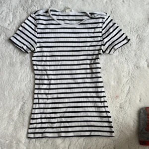 Randig t-shirt från H&M - Säljer en klassisk vit och svart randig t-shirt från H&M. Den är kortärmad och har en ribbad struktur som ger en skön passform. Perfekt för en avslappnad stil.