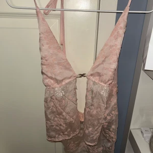 Rosa spetsklänning - Säljer en romantisk rosa topp med spetsdetaljer och djup v-ringning. Klänningen har smala axelband och en elegant design som passar perfekt för speciella tillfällen.super bra nu till sommaren