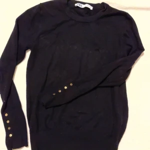 Svart tröja med knappar - Snygg svart tröja från Zara med långa ärmar och dekorativa knappar vid ärmsluten. Perfekt för en stilren look.