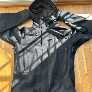 Svart Astral jacka från Haglöfs - Säljer en svart Astral jacka från Haglöfs. Jackan har en praktisk huva och flera dragkedjeförsedda fickor. Perfekt för utomhusaktiviteter med sin funktionella design och slitstarka material. Står M WOMEN men passar alla kön plus sitter bra även på S då jag själv har S och använder den. Ordinarie pris 4000 sek 
