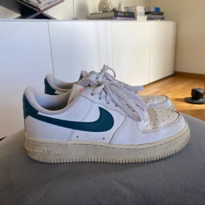Nike Air Force  - Säljer ett par Nike Air Force 1 sneakers i vitt med gröna detaljer. Perfekta för en stilren och sportig look!!