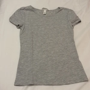 Grå t-shirt från H&M - Säljer en enkel och stilren grå t-shirt från H&M. Den är kortärmad och tillverkad i ett mjukt bomullsmaterial. Perfekt för en avslappnad look.