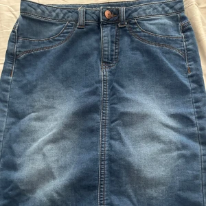 Blå jeanskjol - Snygg blå jeanskjol med klassisk femficksdesign och knappstängning fram. Perfekt för en avslappnad stil. Kjolen har en normal passform och är tillverkad i slitstarkt denimtyg.