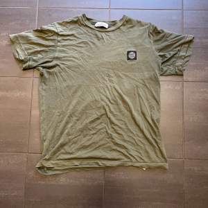 Säljer en olivgrön t-shirt från Stone Island med en liten logga på bröstet. T-shirten har en klassisk rund hals och korta ärmar. Perfekt för en avslappnad stil.